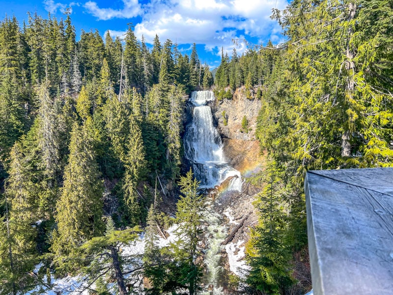 Wasserfall mit den hohen grünen Kiefern auf beiden Seiten und dem Tal darunter.