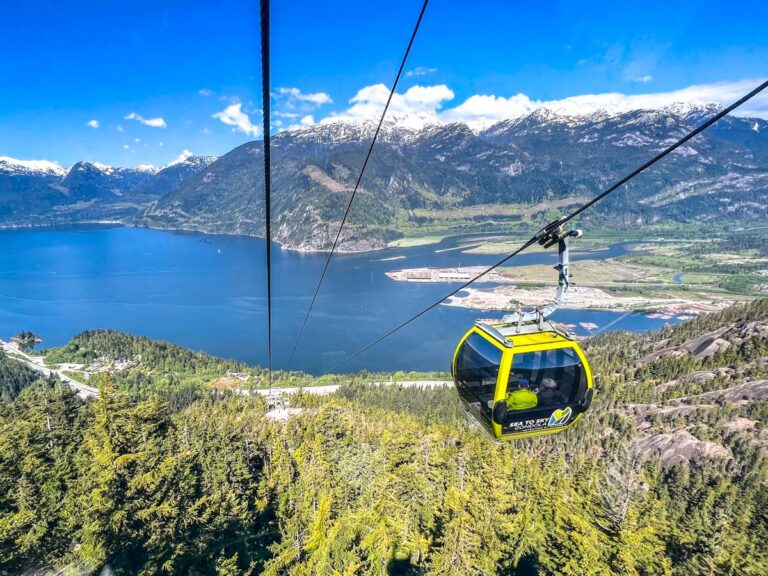 green gondola on cable with small parking lot below and stunning lake and mountains in distance.