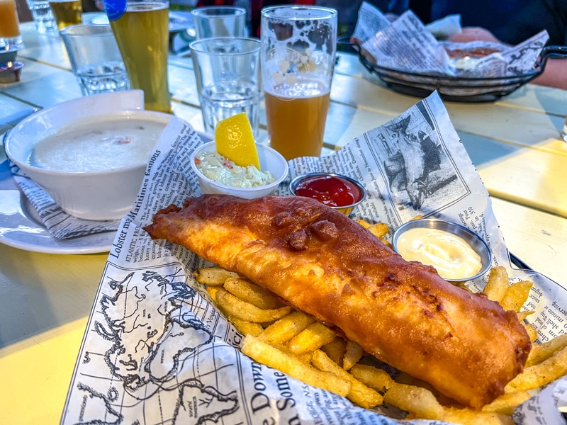 basket of fish and chips on table with beer glasses around.