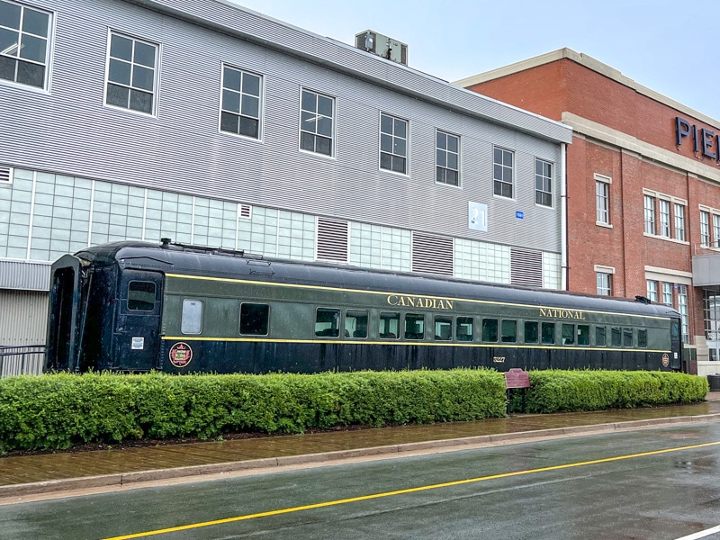 antique green train outside large museum building with green shrubs in front.