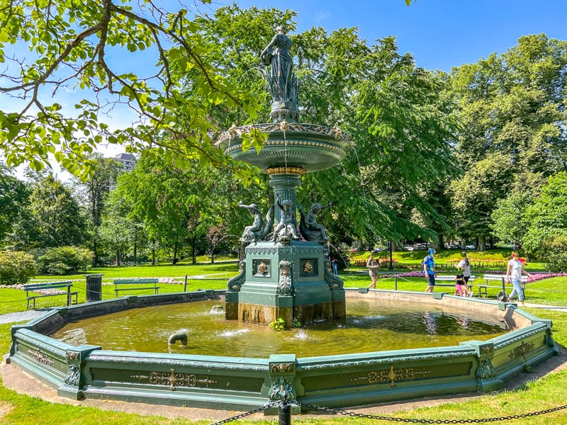 large green water fountain with green trees behind.