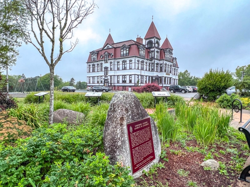 large manor estate house with green shrubs in front and historic plaque embedded into rock.