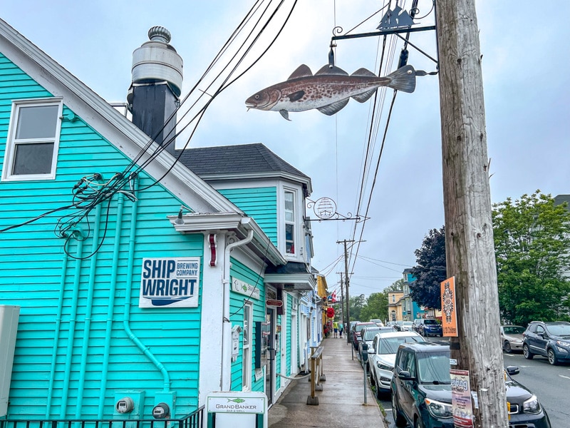 turquoise house with sidewalk out front with fish sign hanging on pole above.