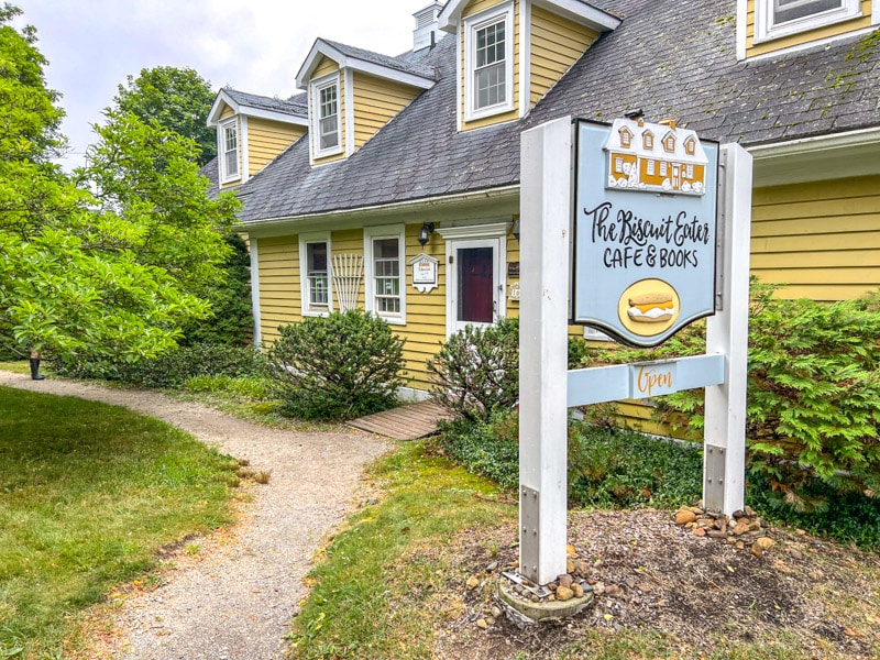 small house cafe with white wooden sign in front beside pathway and grass.