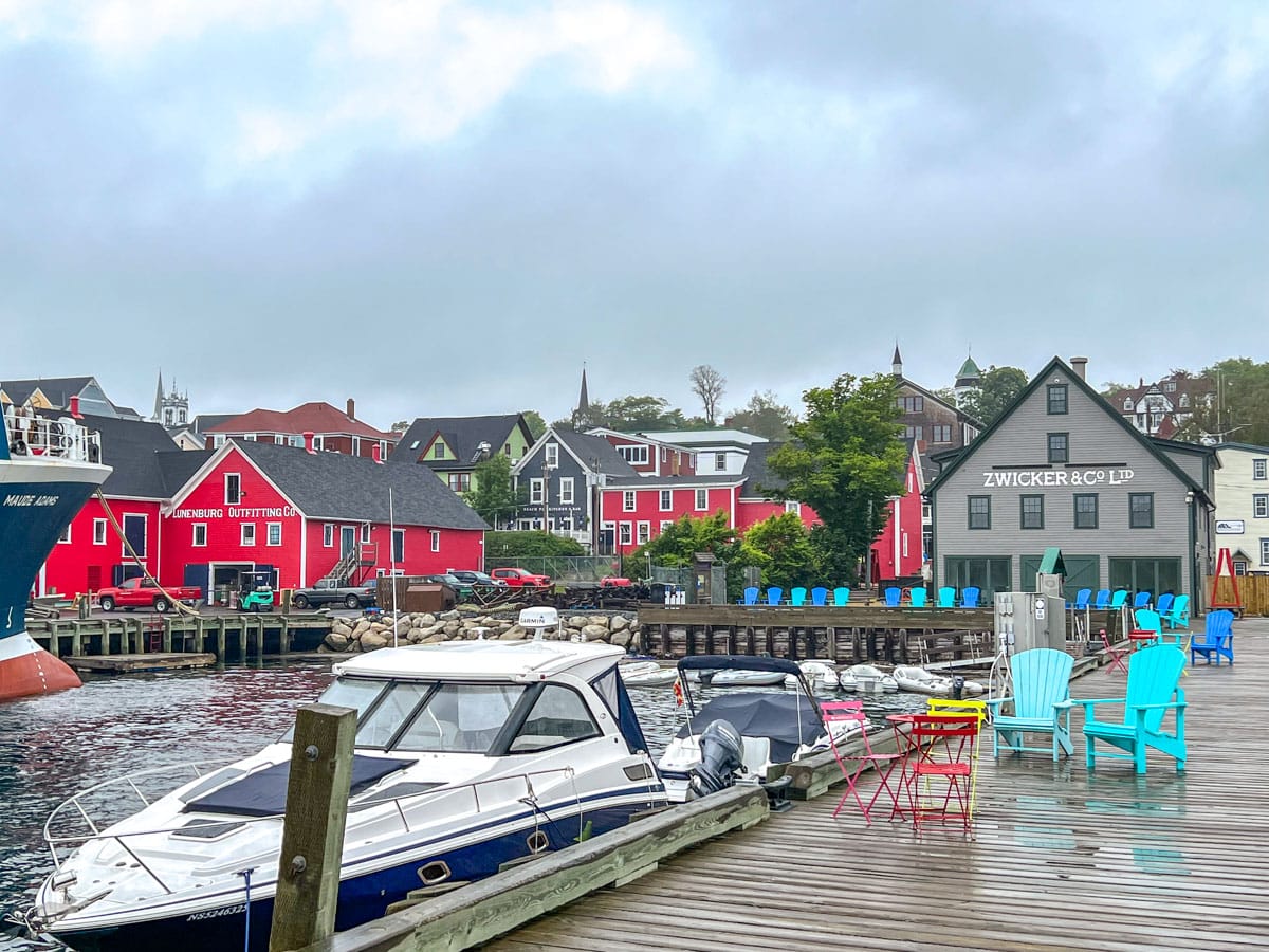 colourful seafront houses with wooden pier in front with chairs and boat.