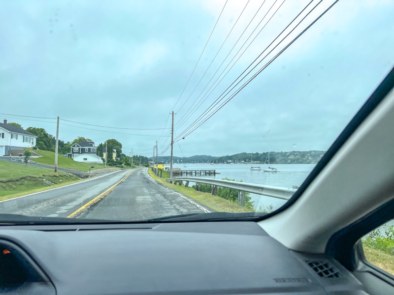 paved road seen through interior of a car with water to the right.