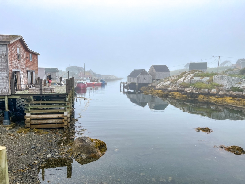 small fishing village with foggy skies and still water on shallow cove in front.