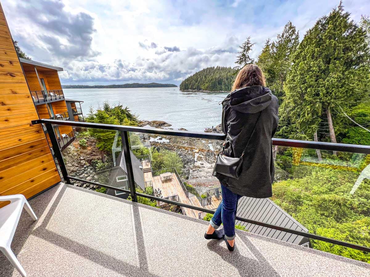large balcony overlooking ocean cove with woman in black jacket standing in front.