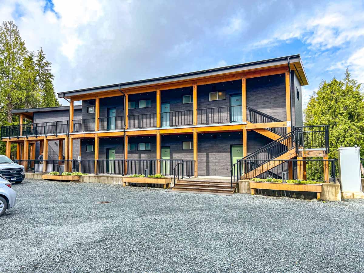 outside shot of black and natural wooden hotel with gravel parking lot in front at duffin cove tofino.