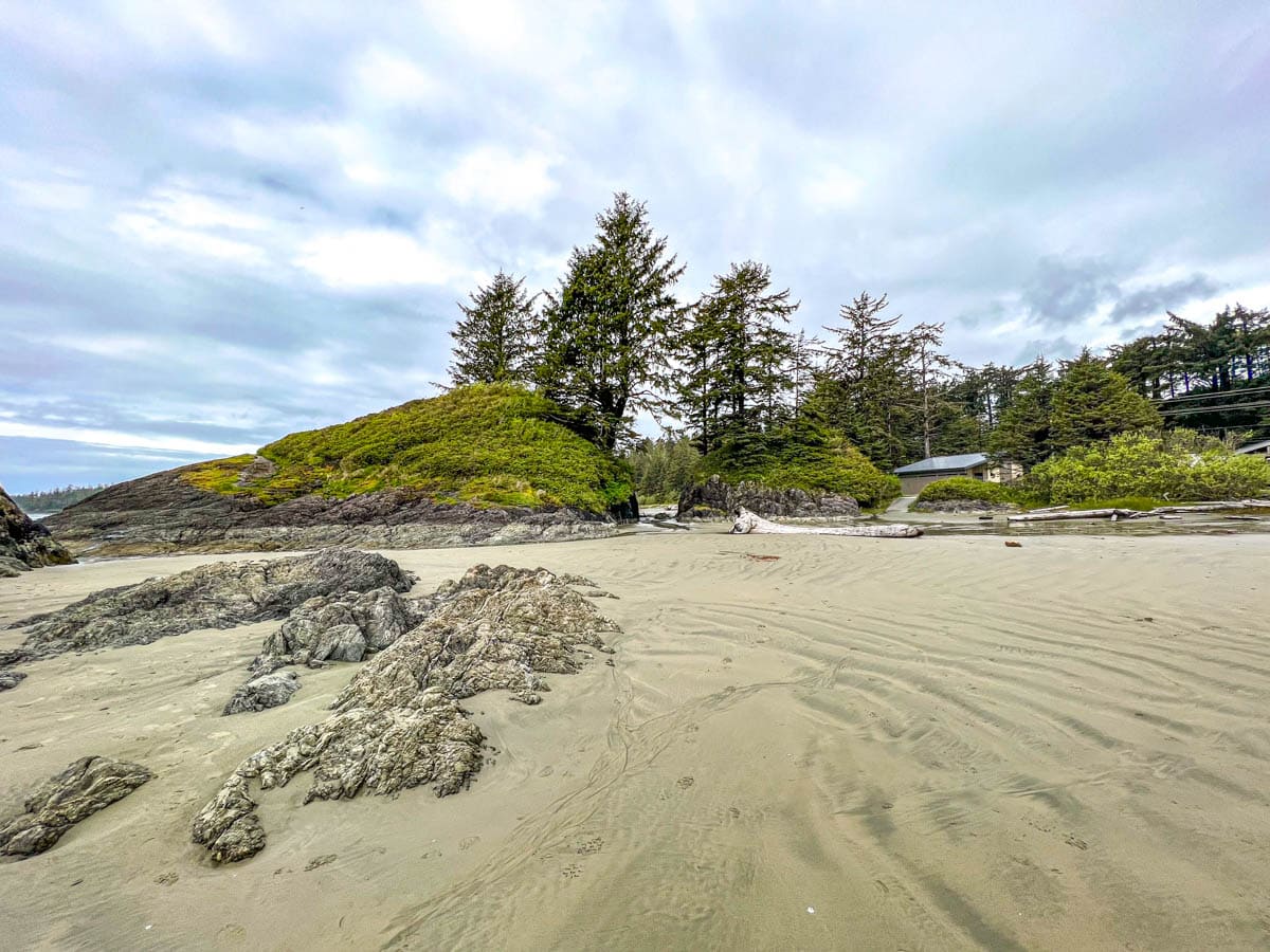 rocky shoreline with trees on top with sand in front at long beach in pacific rim national park in tofino.