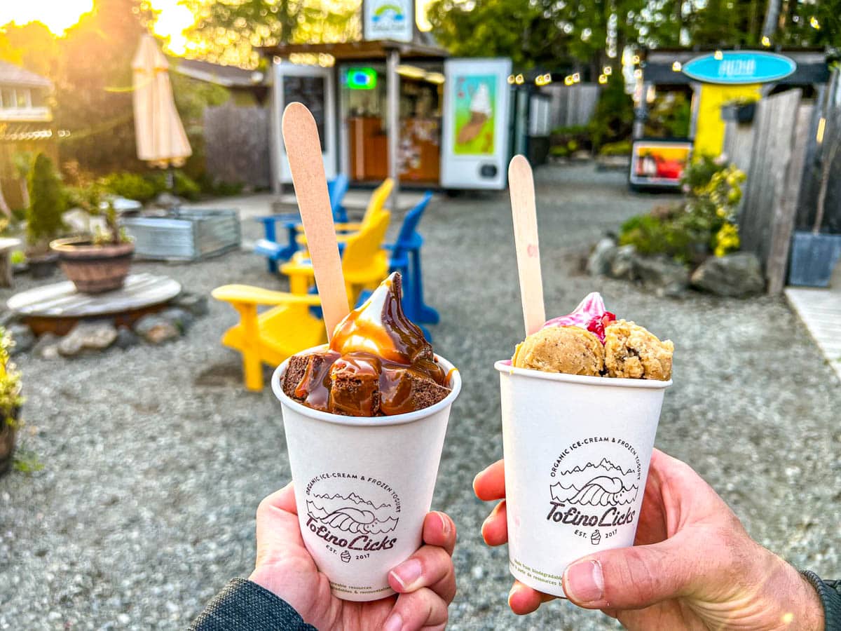two cups of ice cream with spoons sticking out with food trucks and colourful chairs in background.