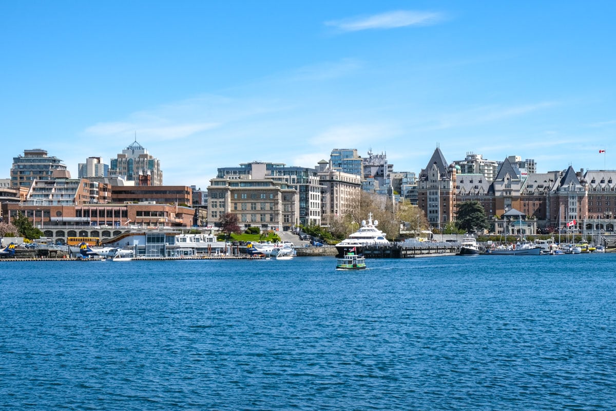 Wasserflugzeuge, die am Pier im Wasser angedockt sind, mit der Innenstadt von Victoria BC im Hintergrund und blauem Himmel darüber.