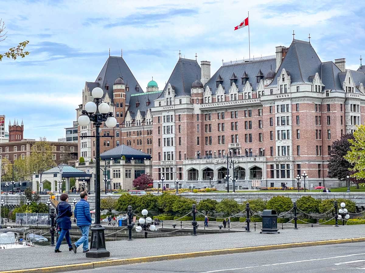 Großes rotes Backsteinhotel in Victoria, BC, mit der kanadischen Flagge darüber und zwei Menschen auf dem Bürgersteig im Vordergrund.
