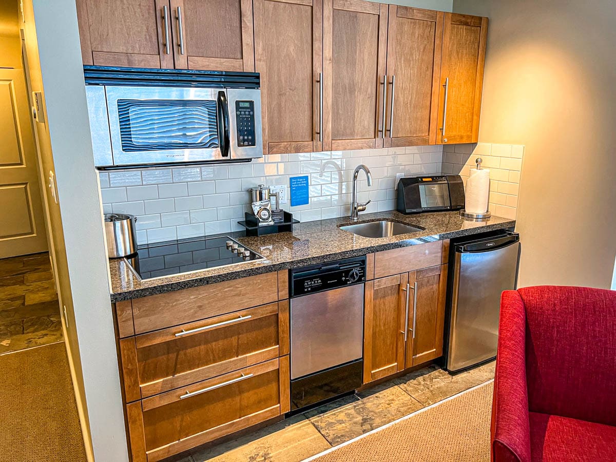kleine Küchenzeile mit Kühlschrank, Mikrowelle und Geschirrspüler mit braunen Holzschränken.