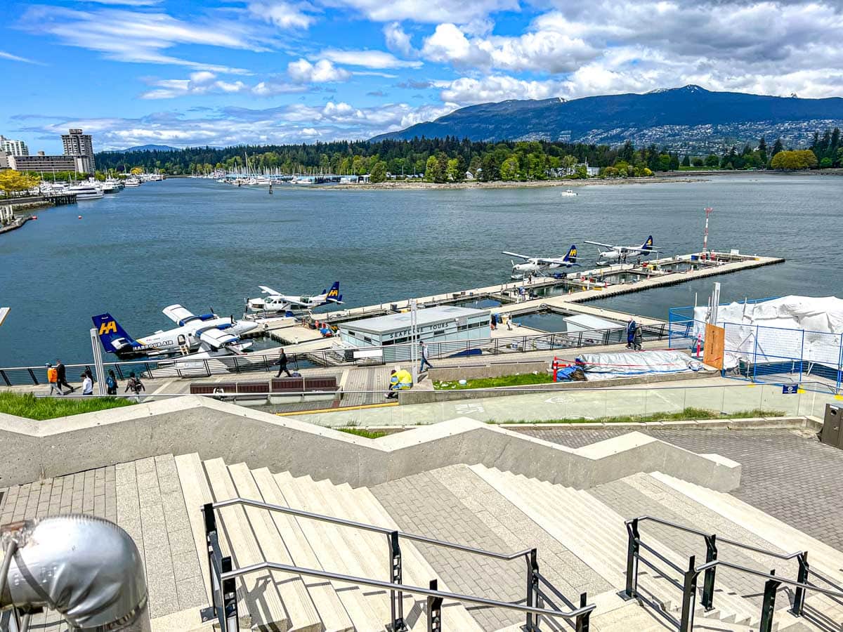 large rectangle dock in harbour with seaplanes parked along it with mountains in behind.