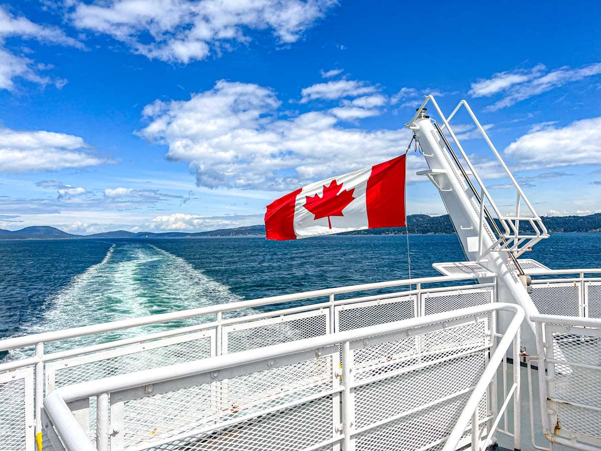canada flag flying off the back of a bc ferry with waves in water trailing behind.
