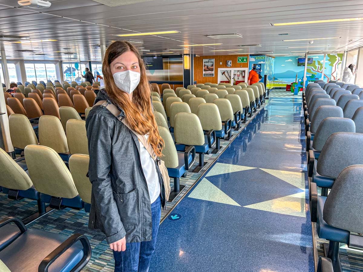 woman standing inside ferry seating area with lots of seats behind her.