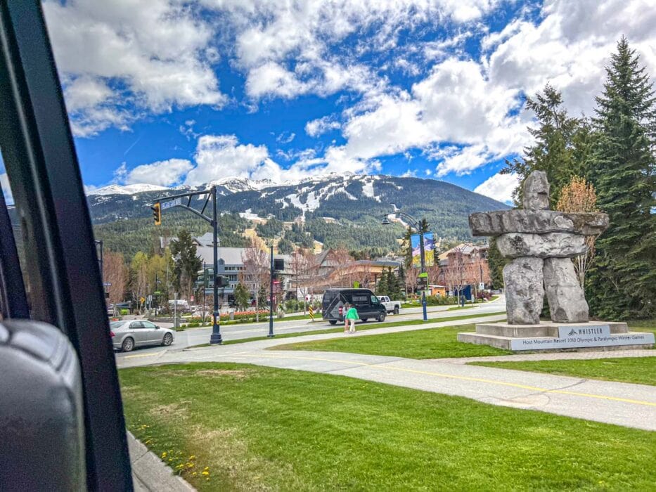 view of sky resort mountain through bus window with statue on grass close by.