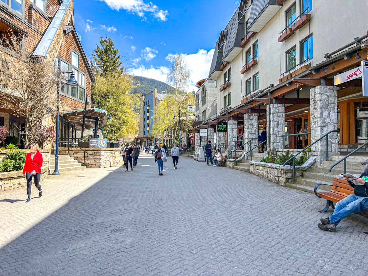 people walking around whistler village shops with blue sky above.