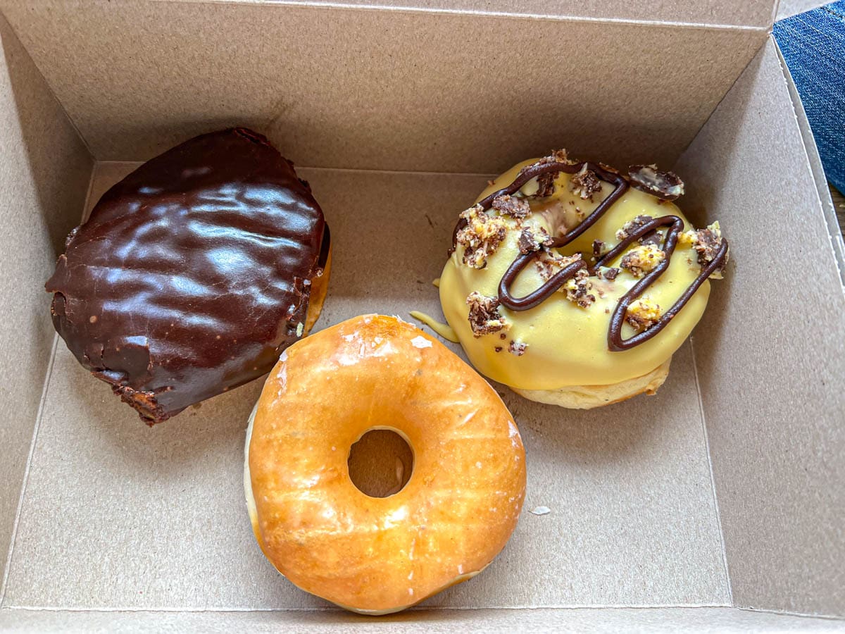 three donuts in cardboard box on person's lap.