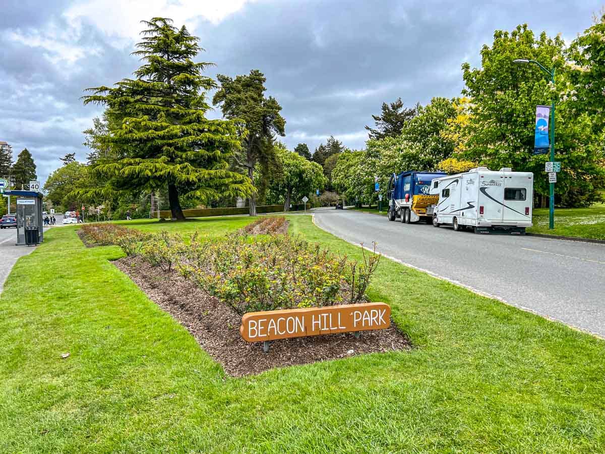 small wooden sign for entrance to green park with trees and rvs behind.
