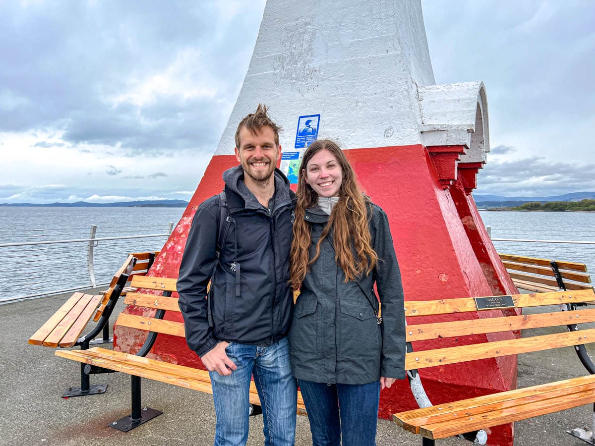 young couple smiling for photo with lighthouse behind them.