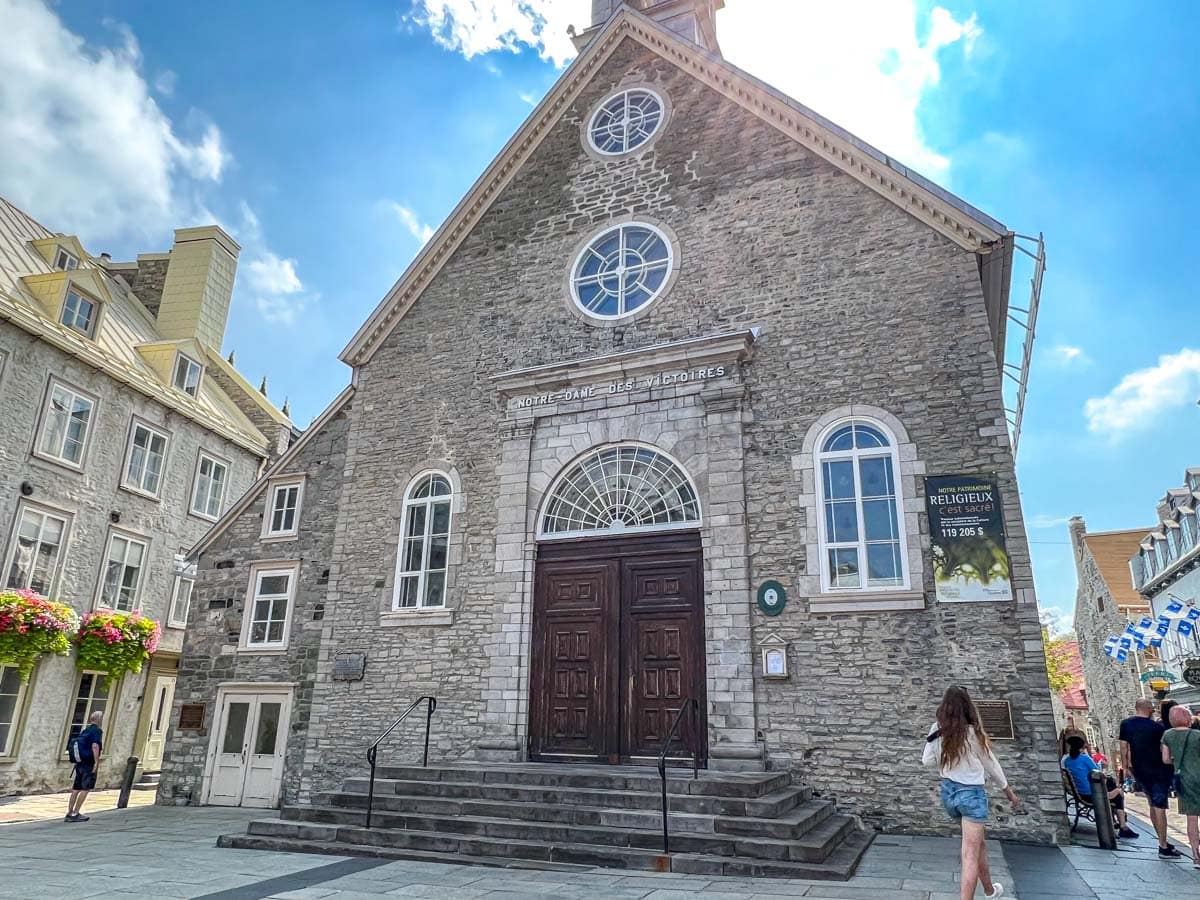 old stone church building overlooking cobblestone square with woman walking by.