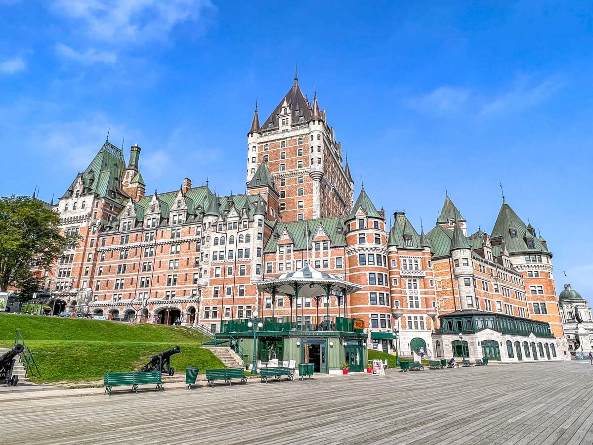 large fancy hotel chateau frontenac with wooden walkway in front and blue sky above.