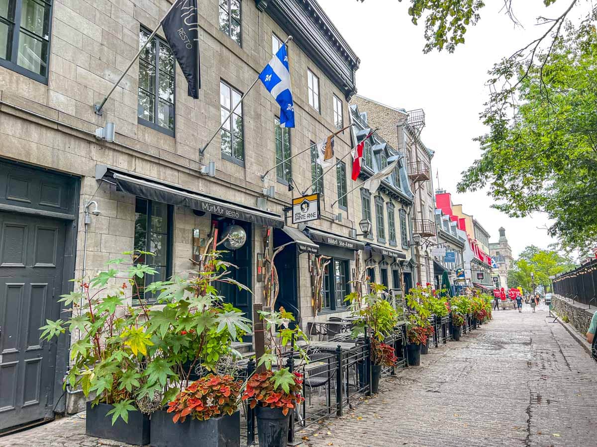 historic stone buildings with flag hanging over sidewalk and plants in front in old quebec.