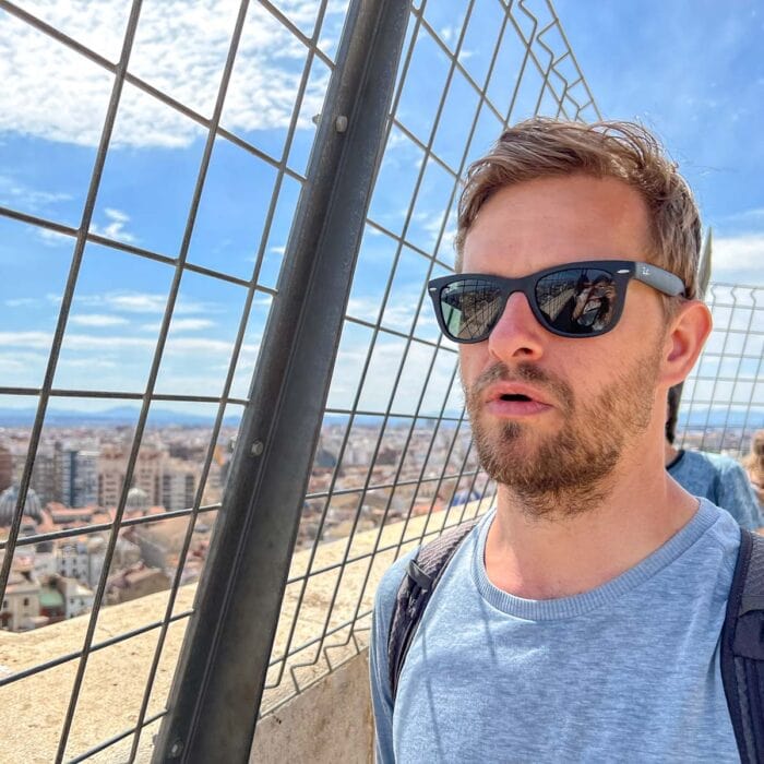 man with black sunglasses and blue shirt posing with spanish city below.