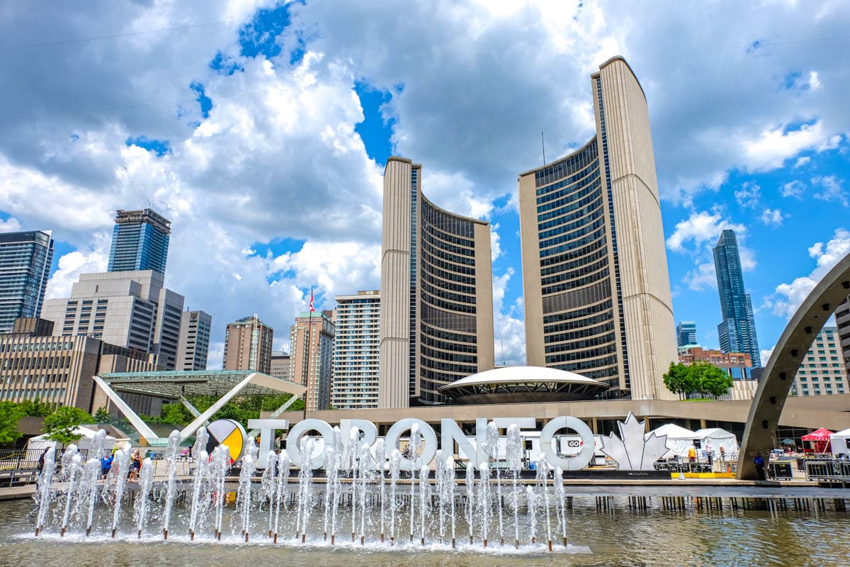 fountain in front of large white letters and curved city hall building at nathan phillips square.